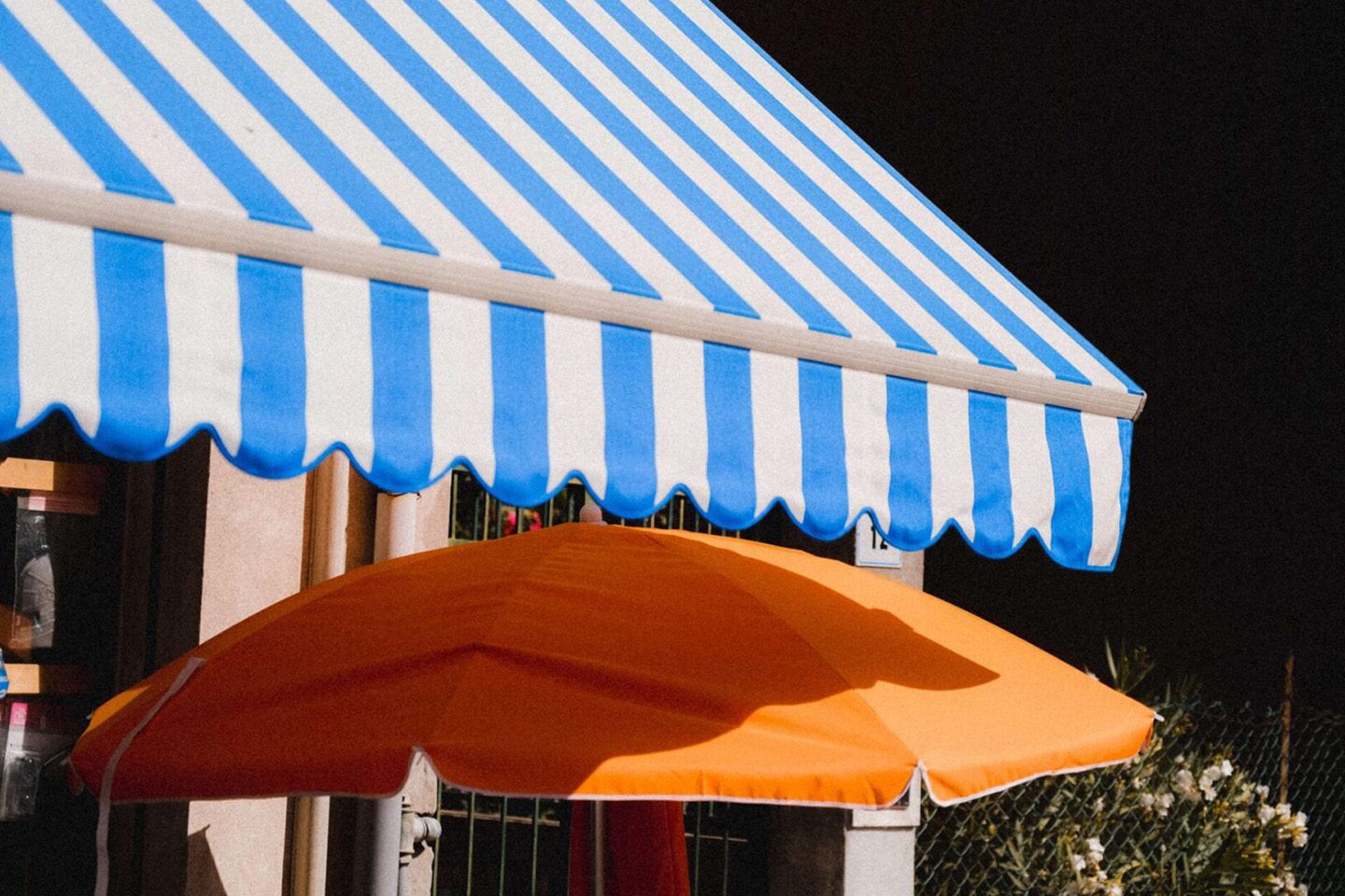 A blue and white awning with an orange umbrella.